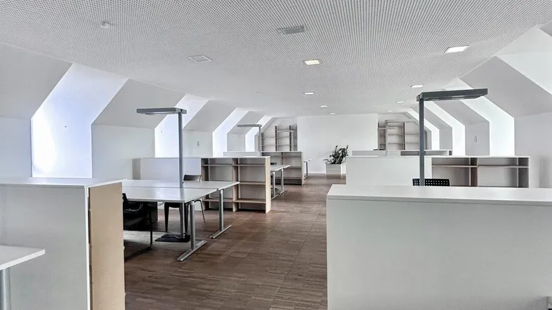 Geräumiges Großraumbüro mit moderner Einrichtung, schrägen Decken und Holzboden, ideal für kreative Arbeitsumgebungen.