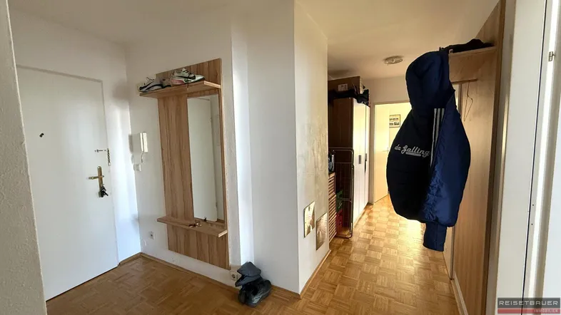Heller Eingangsbereich mit Holzparkettboden und Garderobe mit Spiegel.