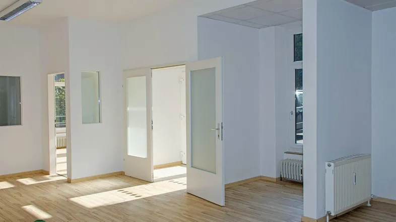 Heller, leerer Raum mit Holzboden, weißen Wänden und mehreren Türen, ideal für Büro oder Wohnen.