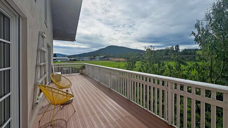 Geräumiger Balkon mit Holzboden und gelben Stühlen, bietet einen weiten Blick auf die grüne Landschaft und Berge.