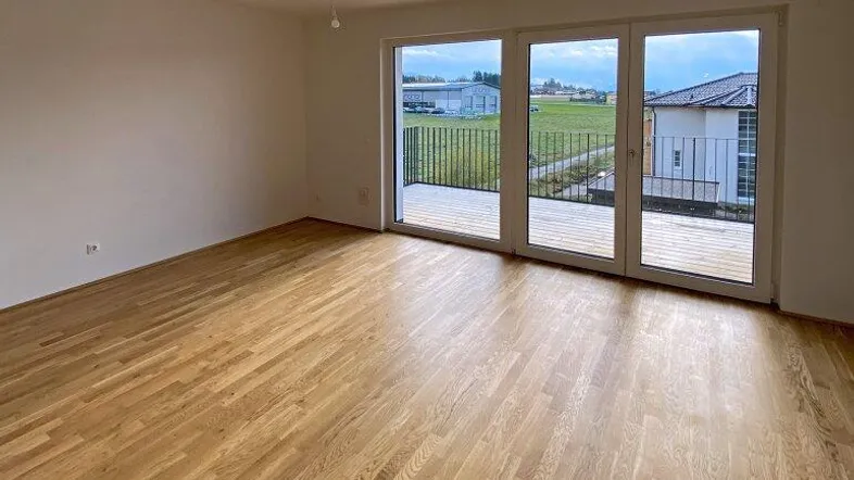 Helles Wohnzimmer mit neuem Parkettboden und Zugang zu einem Balkon mit Blick ins Grüne.