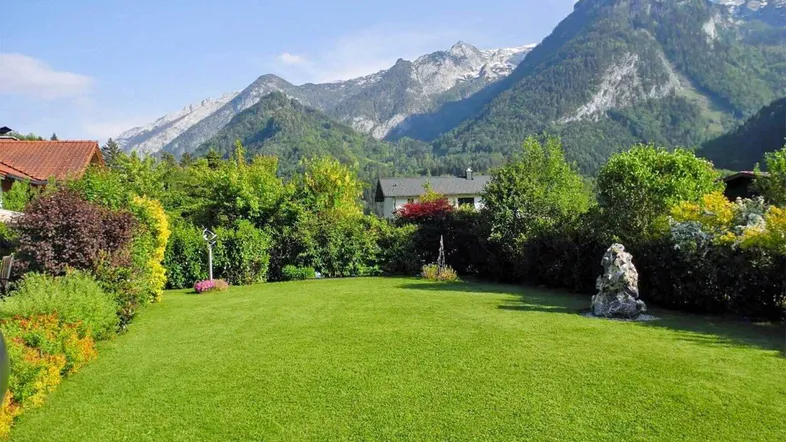 Gepflegter Garten mit weitläufiger Rasenfläche und beeindruckendem Bergblick im Hintergrund.