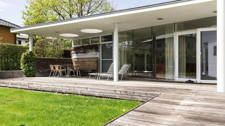Moderne Architektur mit großer Holzterrasse, Liegestühlen und Blick ins Grüne.
