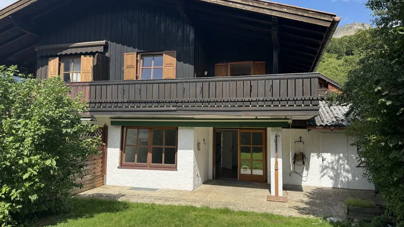 Traditionelles Haus im alpinen Stil mit Garten, Terrasse und Balkon, umgeben von grüner Natur.