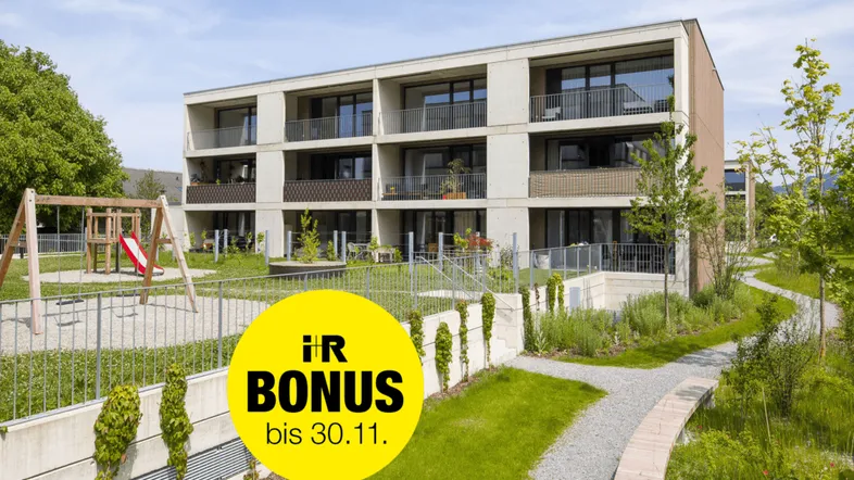 Modernes Mehrfamilienhaus mit Balkonen, Terrassen, weitläufigen Grünflächen und einem Spielplatz.