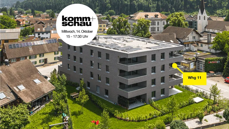 Luftaufnahme eines modernen Wohngebäudes mit Solarpaneelen und umliegender Grünfläche.