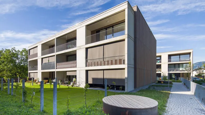 Moderne Wohngebäude mit Balkonen und Außenjalousien, umgeben von Grünflächen.