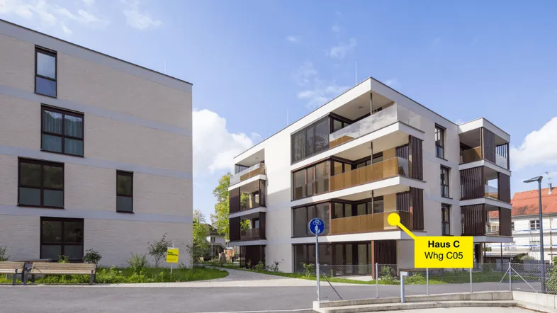 Moderne Mehrfamilienhäuser mit heller Fassade, großen Fenstern und Balkonen unter blauem Himmel.