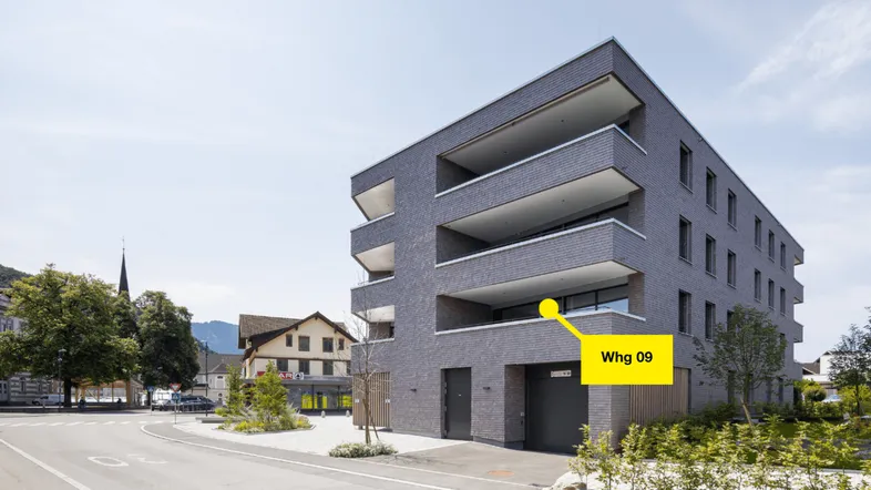 Modernes Mehrfamilienhaus mit Balkonen und schieferähnlicher Fassade in städtischer Umgebung.