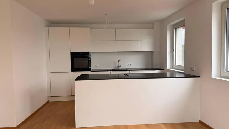 Moderne, offene Küche mit weißen Schränken, schwarzer Arbeitsplatte und Holzboden in neuwertigem Zustand.