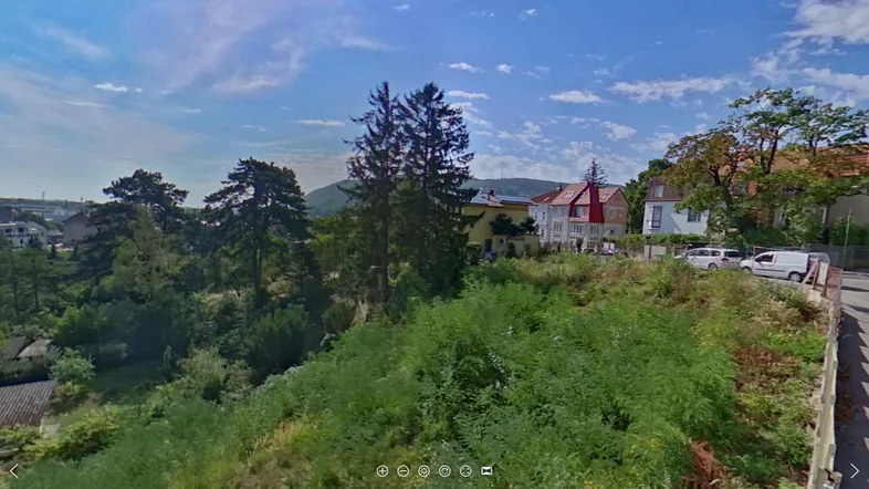 Blick über eine grüne Hügellandschaft mit Bäumen und Häusern unter blauem Himmel.