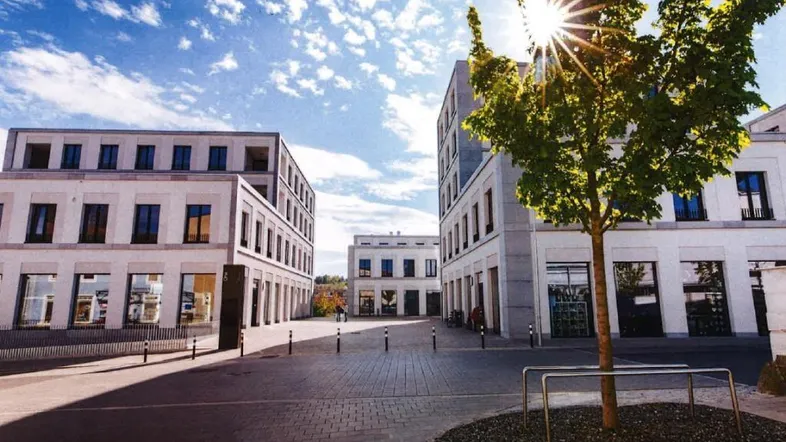 Moderne Geschäftsgebäude an einem sonnigen Platz mit Bäumen und gepflastertem Boden, strahlender Sonnenschein.