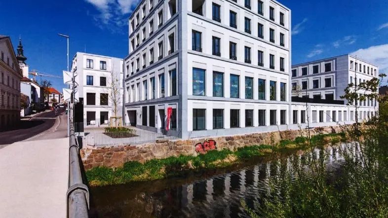 Moderne weiße Gebäude entlang eines Flusses unter blauem Himmel mit Wolken, mit einer Straße im Vordergrund.