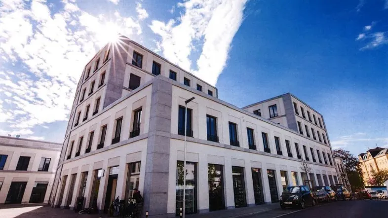 Modernes Gebäude mit weißer Fassade und großen Fenstern unter strahlend blauem Himmel mit Sonnenschein.