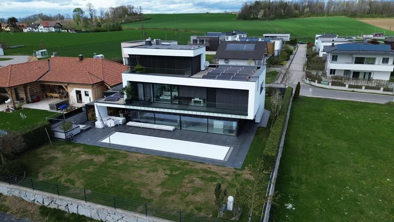Moderne Villa mit Flachdach, Solarpaneelen und einem Pool, umgeben von grünen Feldern.