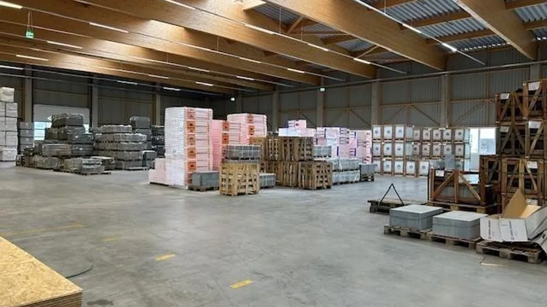 Geräumige Lagerhalle mit hohen Decken, Holzbalken und Oberlichtern, gefüllt mit gestapelten Waren.