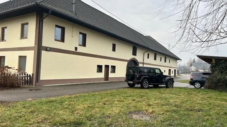 Ansicht des großen, traditionellen Gebäudes mit heller Fassade und dunklem Dach, davor ein geparkter SUV auf dem Rasen.