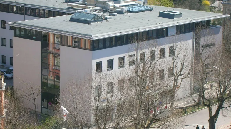 Modernes Bürogebäude mit flachem Dach und großen Fenstern, umgeben von Bäumen und einer Straße.
