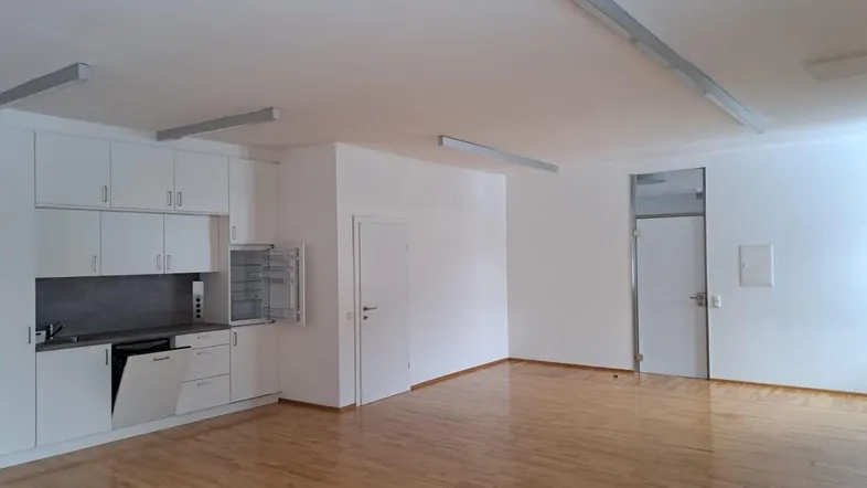Heller, offener Raum mit integrierter Küchenzeile und Holzboden, ideal für Wohn- oder Büronutzung.