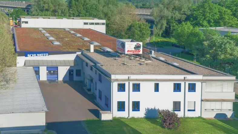 Luftaufnahme eines Gewerbegebäudes mit Flachdach und begrüntem Dachbereich, umgeben von Bäumen.