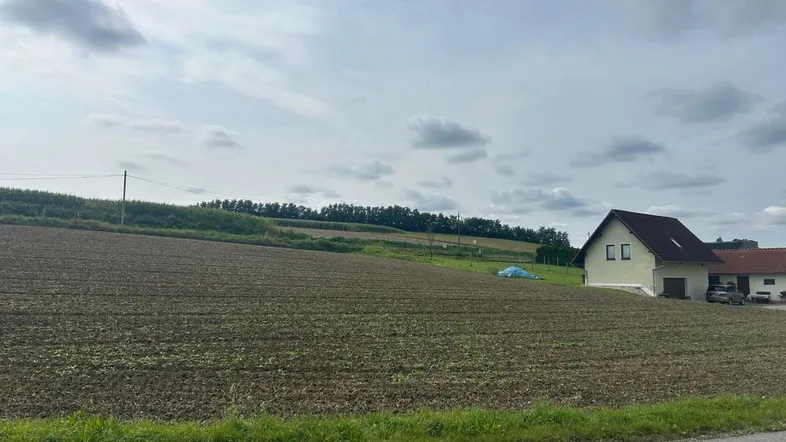 Blick auf ein weites Feld mit einem Wohnhaus im Hintergrund unter bewölktem Himmel.