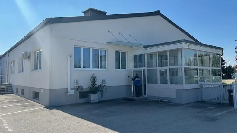 Ansicht des Gebäudes von außen mit einem Wintergartenanbau und einem gepflasterten Parkplatzbereich.