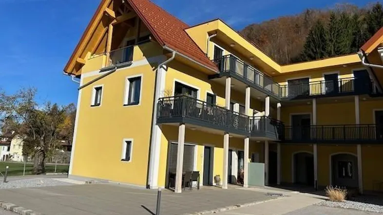 Gelbes Mehrfamilienhaus mit roten Ziegeldächern und Balkonen unter blauem Himmel.