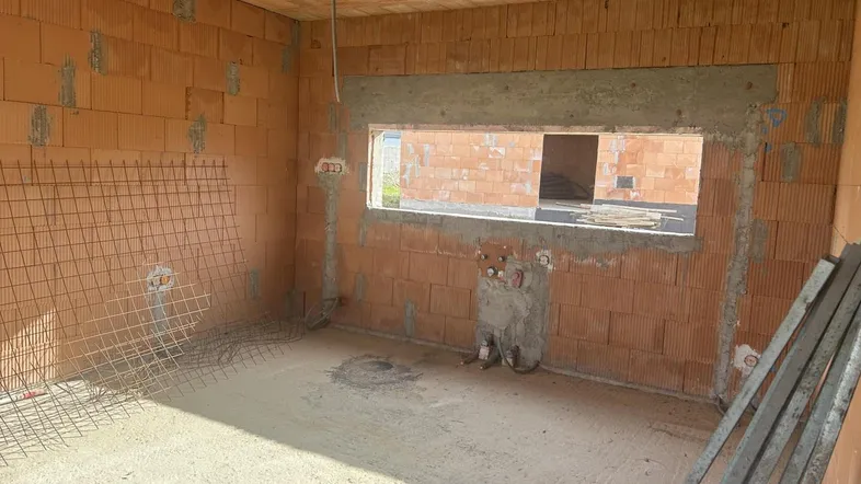 Rohbau eines Raumes mit Ziegelwänden, Fensteröffnung und sichtbaren Installationen, bereit für den Innenausbau.