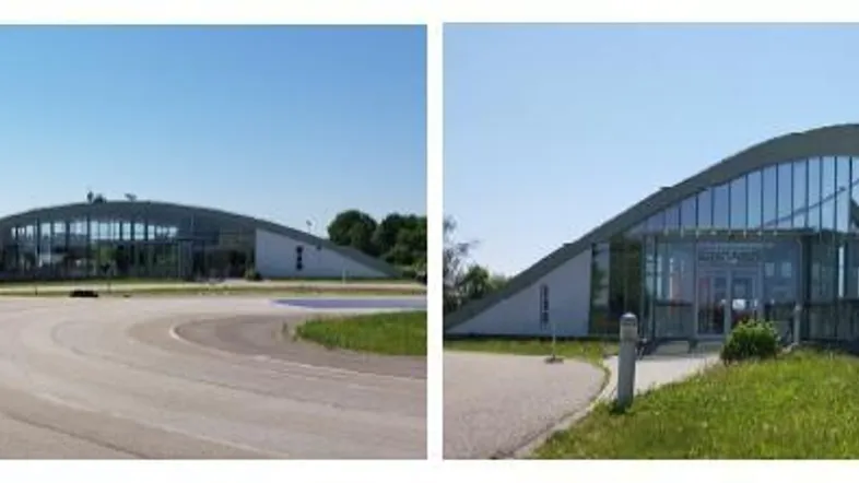 Modernes Gebäude mit geschwungenem Gründach und großer Glasfassade unter blauem Himmel.