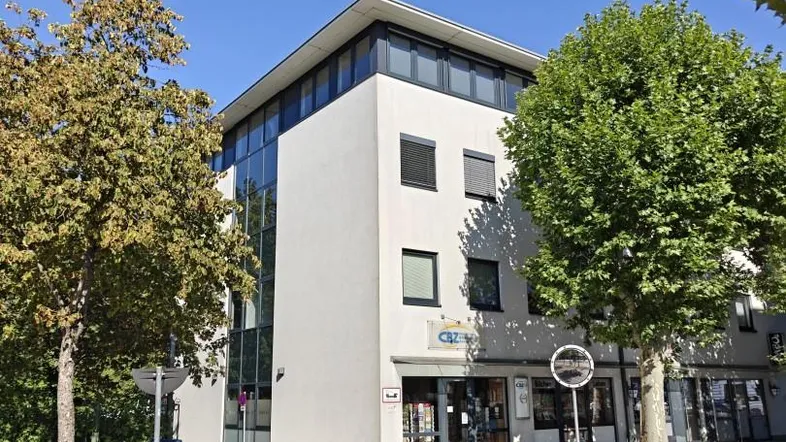 Modernes Geschäftsgebäude mit großen Fensterfronten und klaren Linien, umgeben von Bäumen an einer Straße.