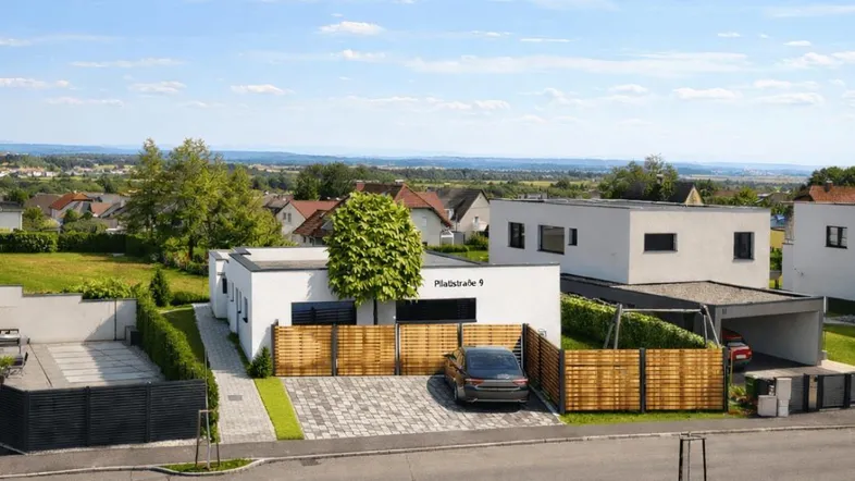 Moderne Neubauvilla mit weißer Fassade, gepflegter Auffahrt und weitem Blick über die Landschaft.