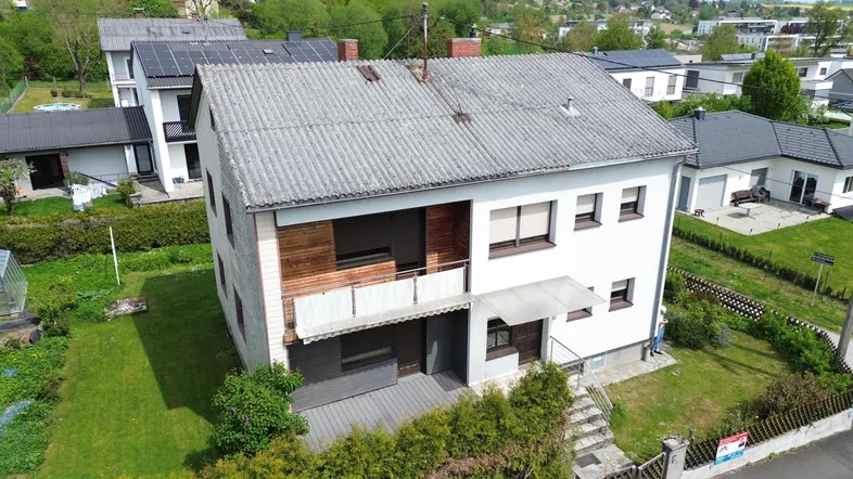 Luftaufnahme eines Einfamilienhauses mit Garten, Balkon und umliegender Wohnbebauung.