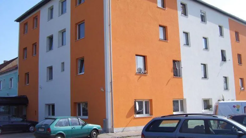 Mehrstöckiges Gebäude mit auffälliger orange-weißer Fassade und geparkten Autos davor.