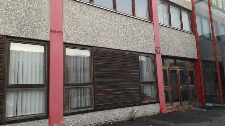 Fassade eines Geschäftsgebäudes mit großen Fenstern, Holzelementen und roten Stützen, die eine ältere Bauweise zeigen.