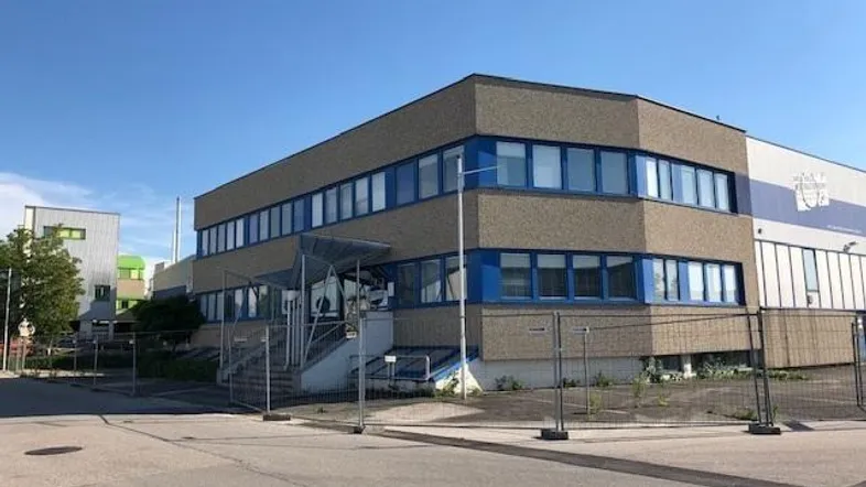 Modernes Bürogebäude mit blauen Fensterrahmen und gepflegter Fassade unter klarem Himmel.
