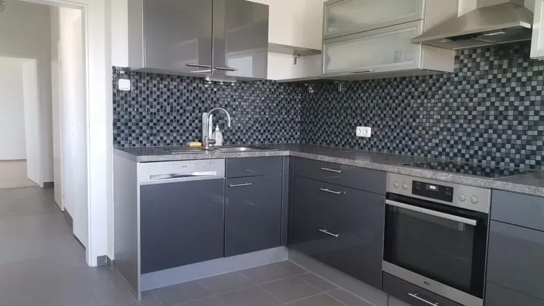 Moderne Einbauküche in Grau mit Mosaikfliesen, integrierten Geräten und Fliesenboden.
