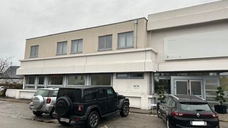 Gebäudeansicht eines Gewerbeobjekts mit Parkplätzen davor unter bewölktem Himmel.