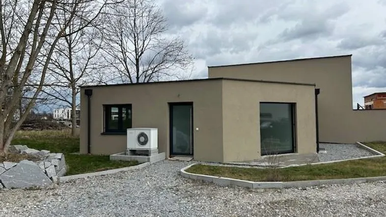 Modernes Einfamilienhaus mit Flachdach und beigefarbener Fassade unter bewölktem Himmel.