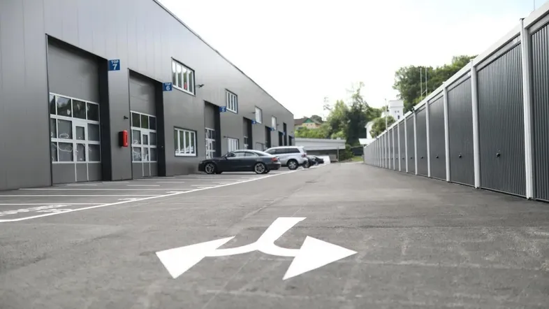 Moderne Gewerbegebäude mit mehreren Garagentoren, Parkplätzen und Lagerboxen entlang einer Zufahrt.