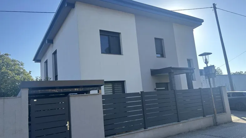 Moderne Hausfassade mit klaren Linien und einem eleganten Zaun unter blauem Himmel.