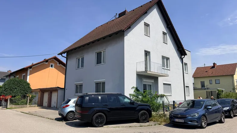 Mehrfamilienhaus mit heller Fassade, Satteldach und kleinem Balkon in einer Wohnsiedlung.