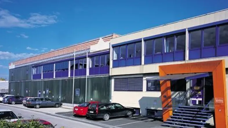 Außenansicht eines modernen Gewerbegebäudes mit blauen Fensterläden und einem markanten orangefarbenen Eingangsbereich.