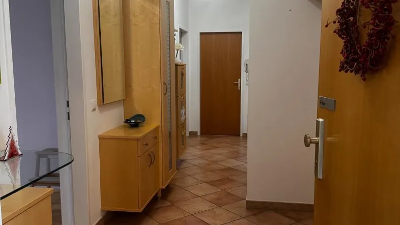 Heller Flur mit Terrakotta-Fliesenboden und Holzmöbeln, der zu weiteren Räumen führt.