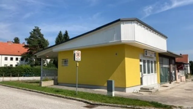 Gelbes Gebäude mit weißem Dach und Vordach, umgeben von einer Straße und Grünflächen unter blauem Himmel.