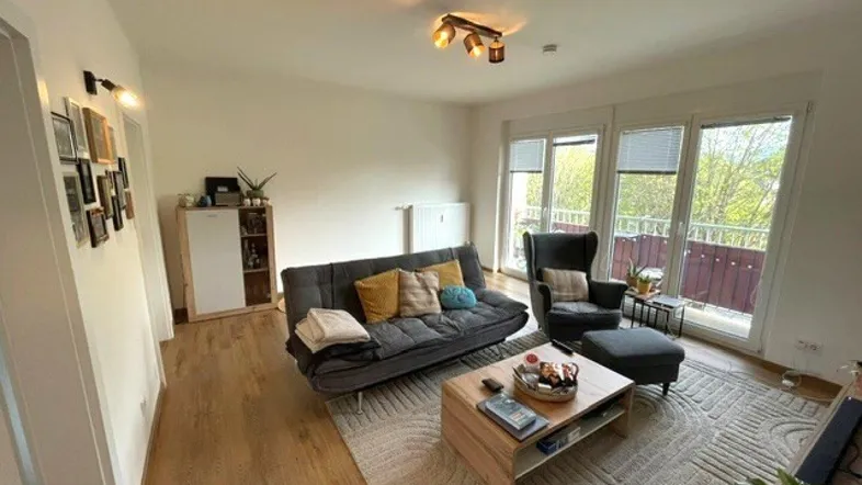 Helles Wohnzimmer mit modernem Sofa, Holzboden und Zugang zu einem Balkon mit grüner Aussicht.