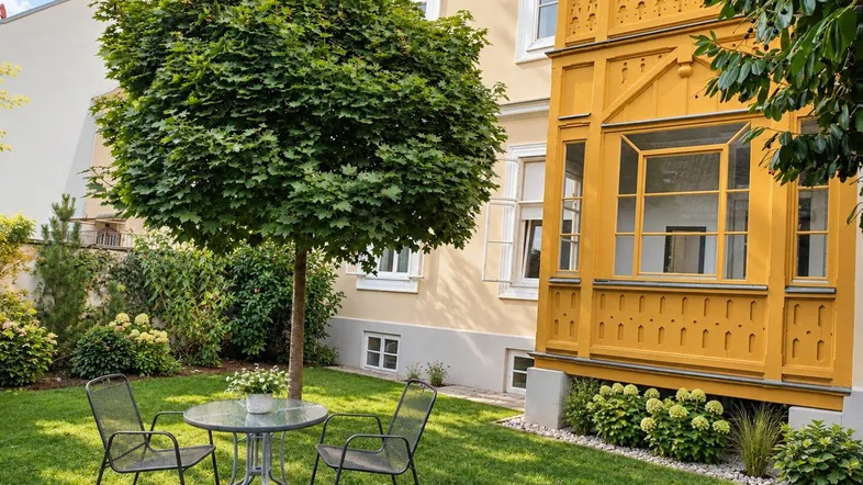 Gepflegter Gartenbereich mit Sitzgelegenheiten und Blick auf die historische Gebäudefassade mit gelbem Erker.