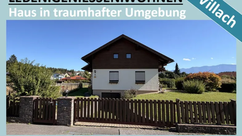 Hausfassade mit Garten, Zaun und Bergblick in sonniger Umgebung von Villach.