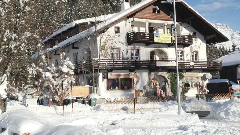 Alpines Gebäude mit verschneitem Dach und Balkonen in winterlicher Berglandschaft.