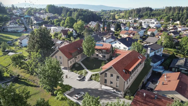 Luftaufnahme der modernen Wohnanlage in grüner, hügeliger Umgebung mit Satteldächern und Photovoltaikanlagen.