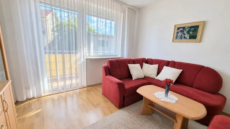 Helles Wohnzimmer mit rotem Ecksofa, Holzboden und Zugang zu einem Balkon.
